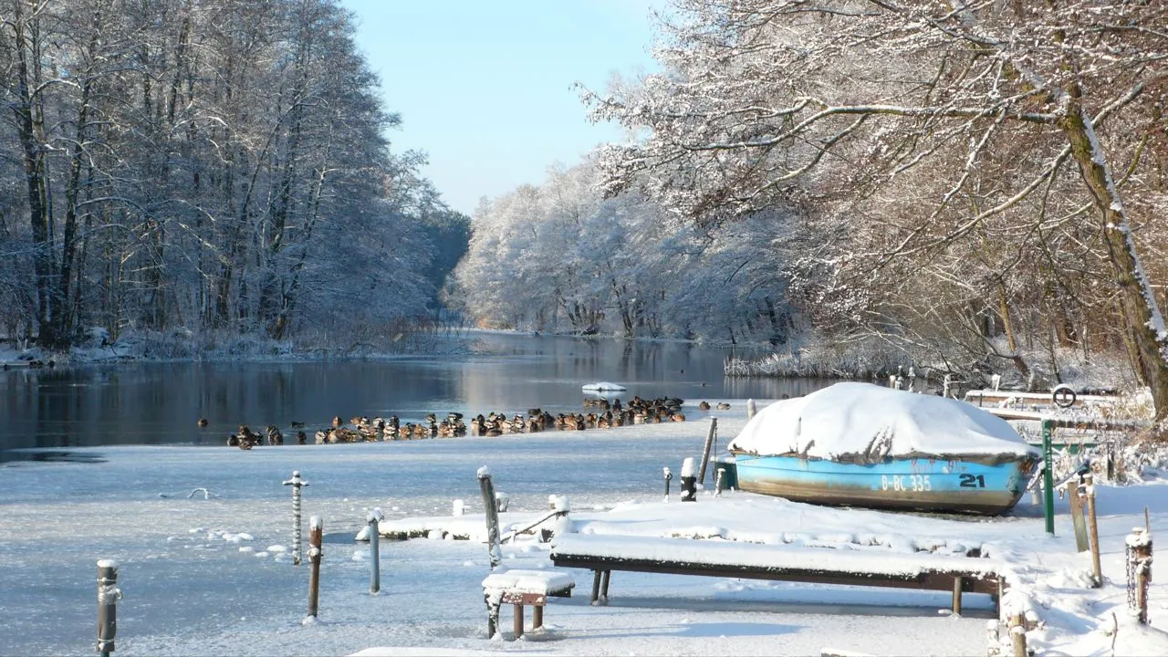 Verschneites Boot am zugefrorenen Spreeufer im Winter
